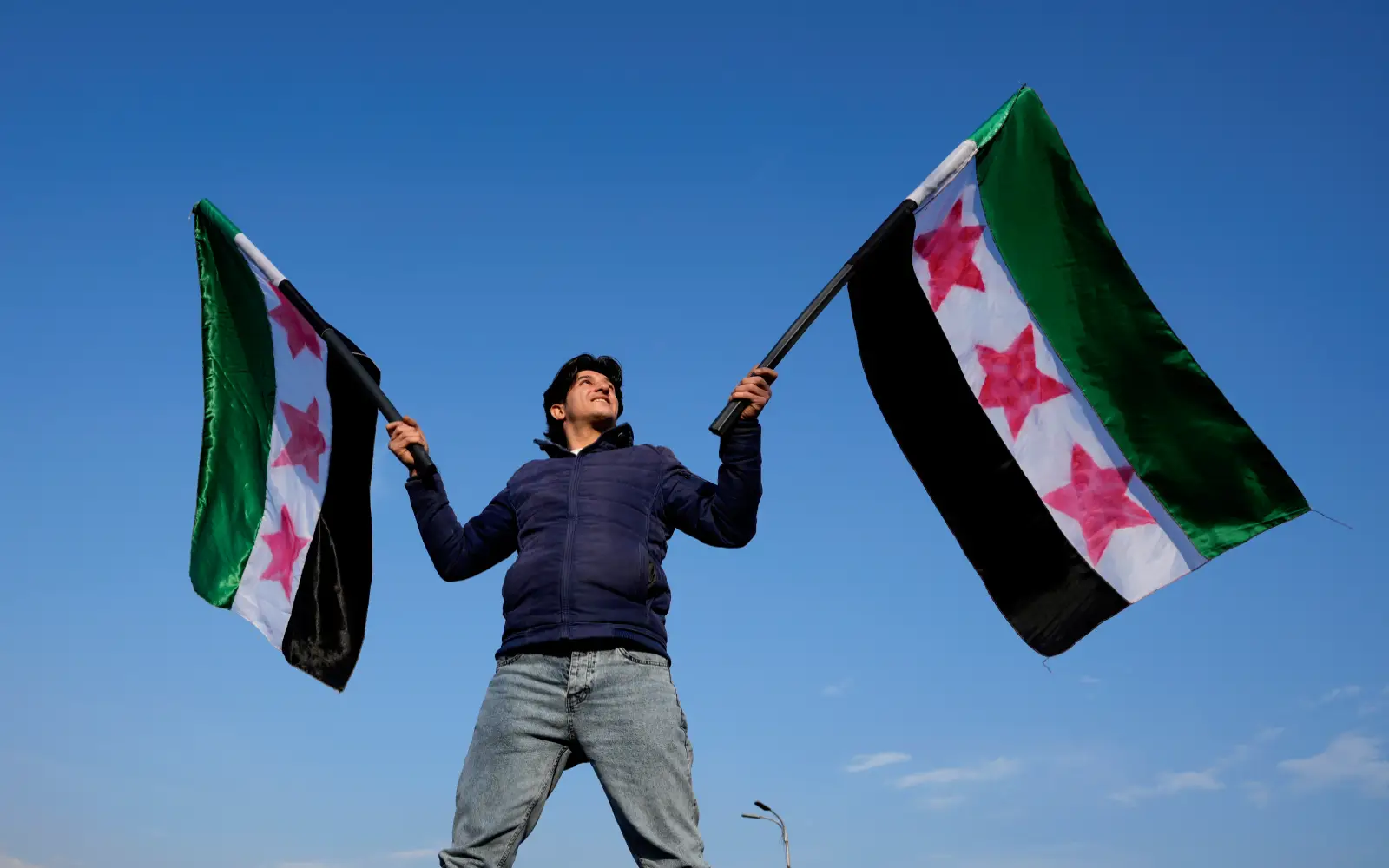 Une personne syrienne brandissant les drapeaux « révolutionnaires » en célébrant l'éviction du gouvernement de Bashar al-Assad © AP